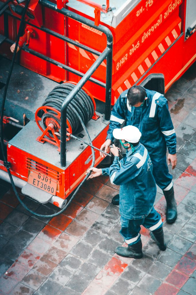 Two Men In Blue Uniforms Standing Beside A Fire Truck